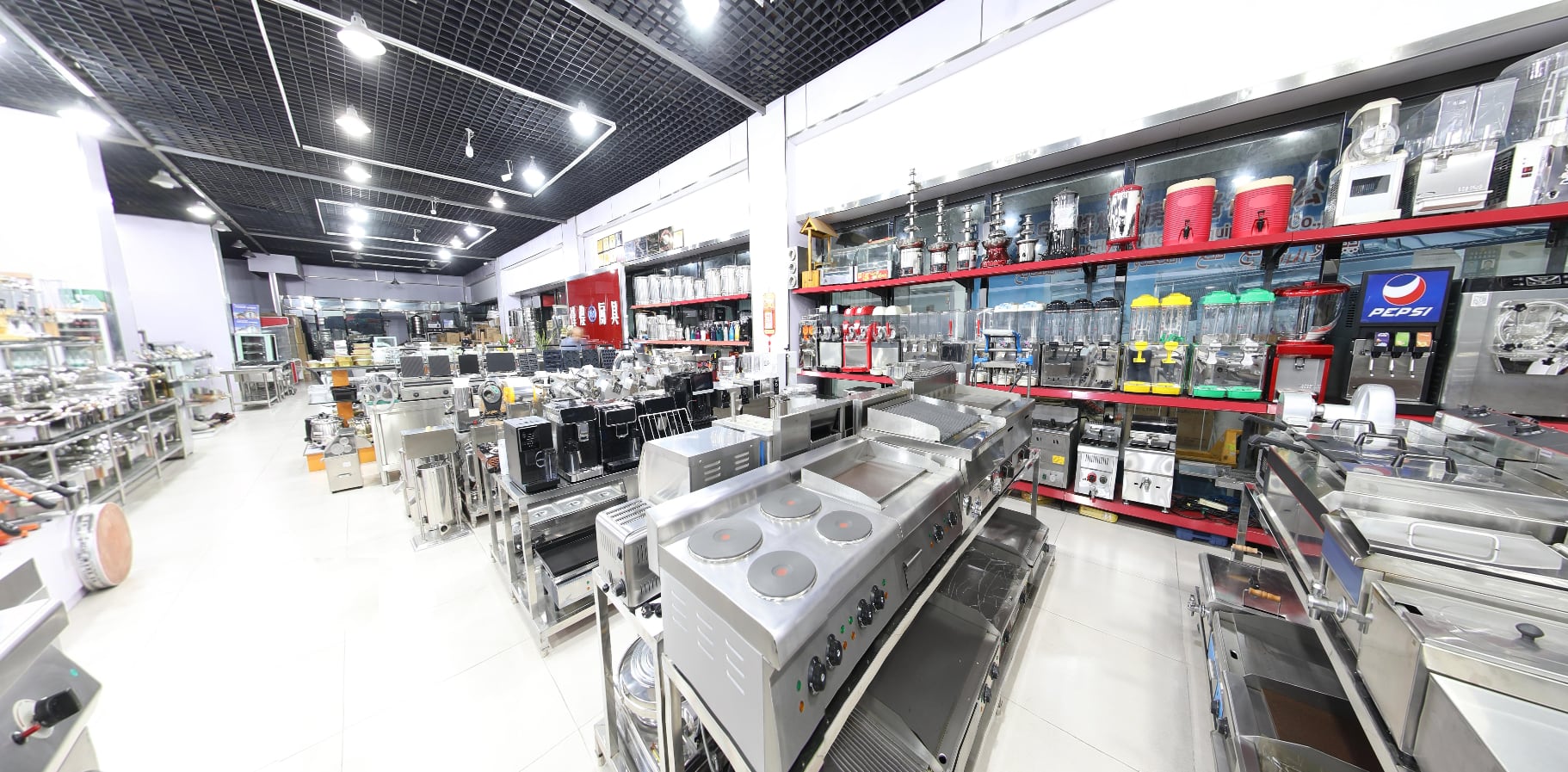 Panorama of the XFH Kitchen showroom floor: cooking ranges in the foreground, display chillers, juice dispensers and a soft-serve line along the wall
